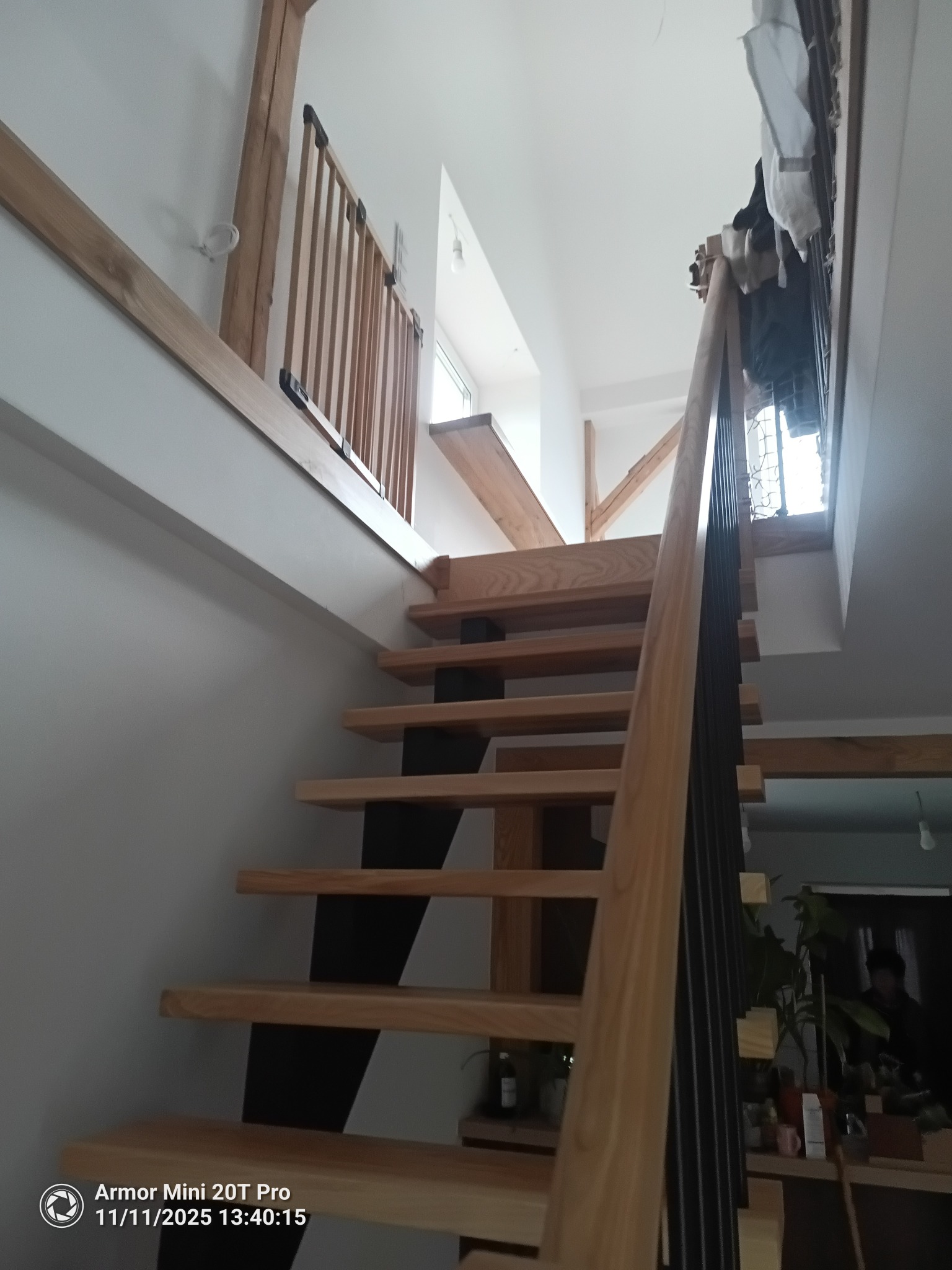 Drewniane schody z czarnymi wspornikami, widok z dołu, w jasnym wnętrzu z elementami drewnianymi. Balustrada z pionowych szczebli.