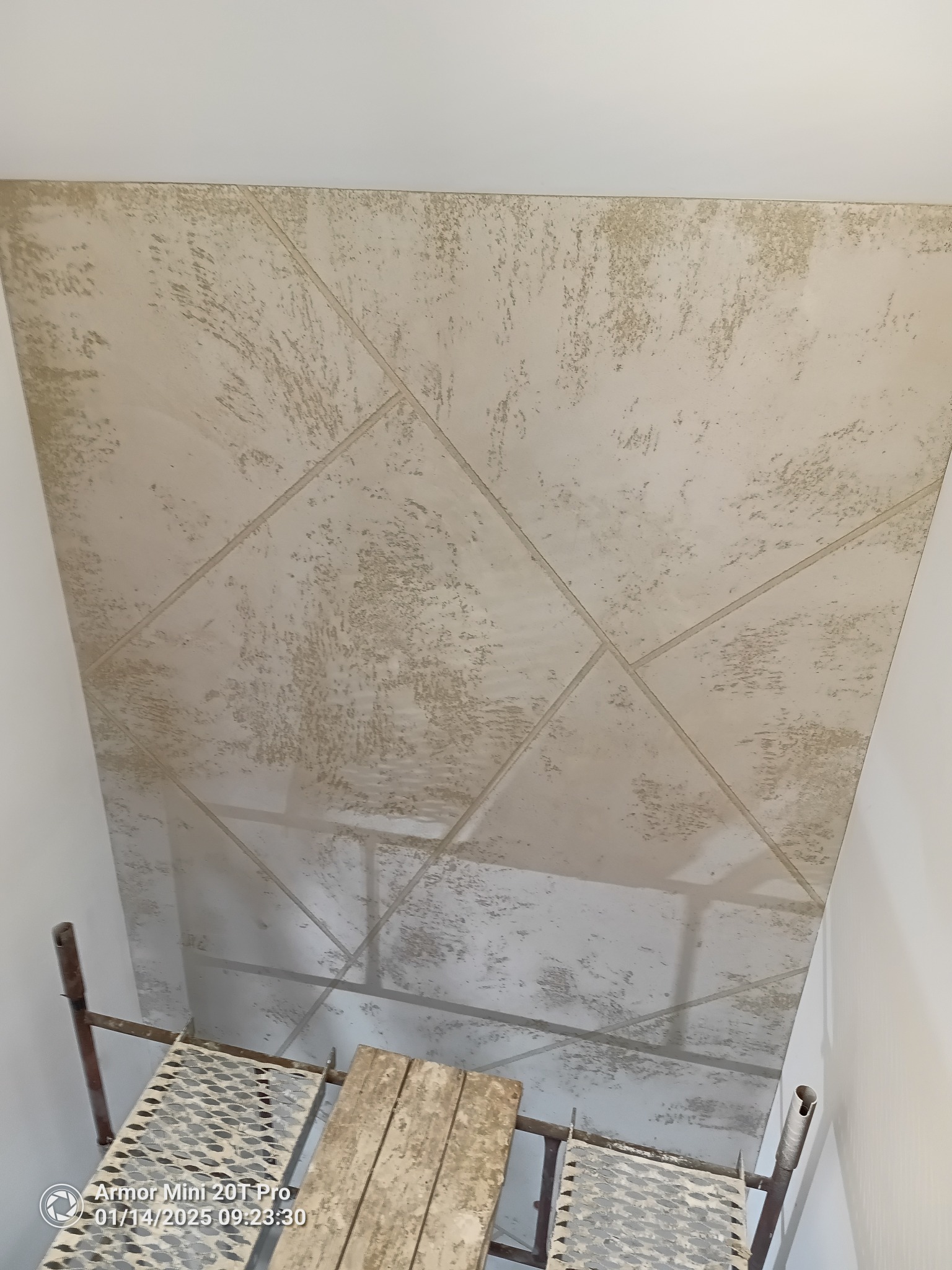 Dekoracyjna ściana z efektem betonu, podzielona geometrycznie listwami. Widoczny fragment rusztowania malarskiego. Wykończenie wnętrza w surowym stylu.