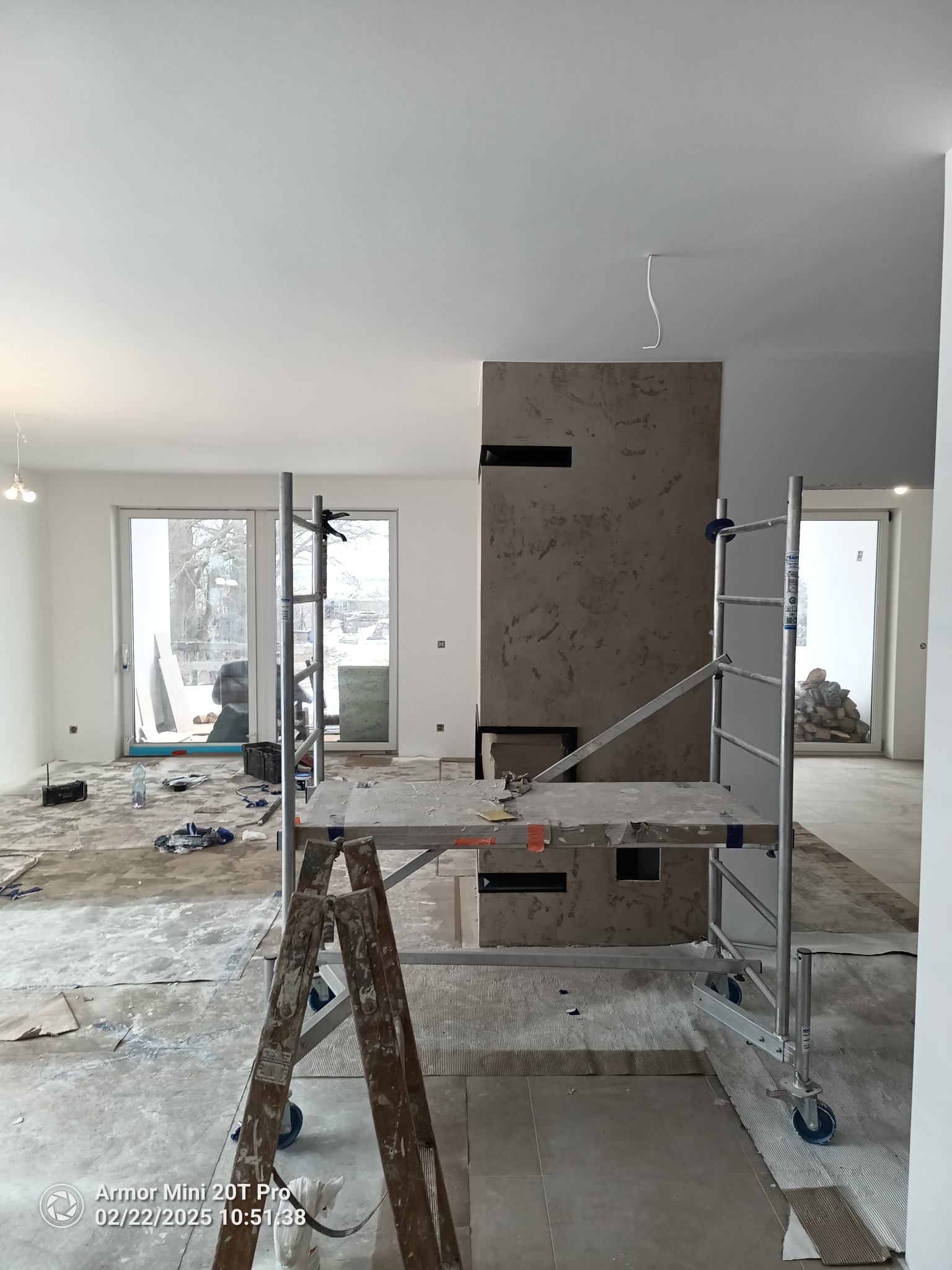 Wnętrze w trakcie remontu: rusztowanie na pierwszym planie, ściana z dekoracyjną fakturą w tle, podłoga przygotowana do dalszych prac wykończeniowych.