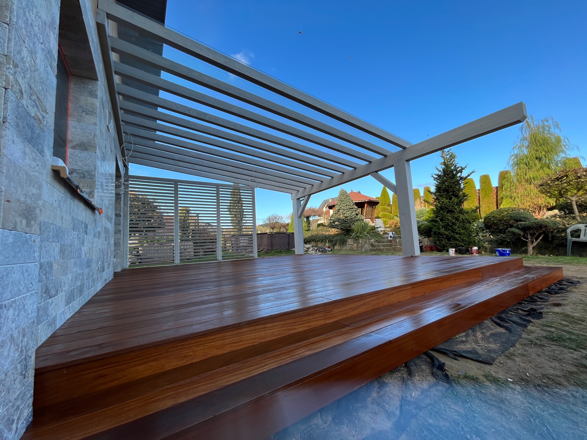 Nowoczesny taras z drewna egzotycznego z szarą pergolą, widok z dołu, podkreślający strukturę drewna i minimalistyczny design konstrukcji.