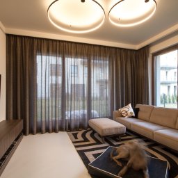 Pasadena home & deco - Nowoczesny salon z miedzianymi zasłonami o splocie plecionki, szyny sufitowe KS białe. Widoczny fragment sofy, stolika i dywanu w geometryczne wzory.