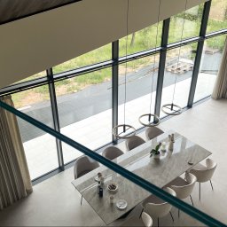 Pasadena home & deco - Wysokie okna z beżowymi zasłonami Broadway 17 na czarnych karniszach Loft 25, widok z góry na jadalnię z marmurowym stołem i krzesłami. Lekki i elegancki wystrój.