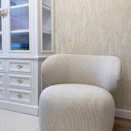 Pasadena home & deco - Beżowy fotel Riley z tapicerką w prążki, na tle ściany w liście i białej komody z przeszkloną witryną. Widoczne logo firmy Pasadena Home & deco.