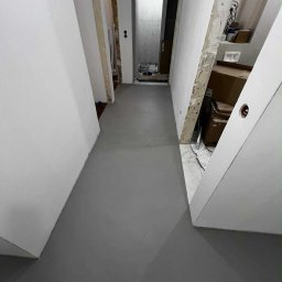 Decoratorium - Szara, gładka posadzka w korytarzu w trakcie remontu. Widoczne surowe ściany i przygotowania do dalszych prac wykończeniowych. Minimalistyczny design.