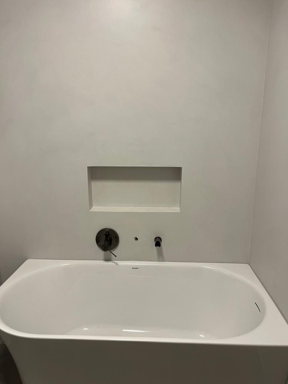 Minimalistyczna łazienka w Kobyłce: biała wanna Duravit, ściana z wnęką i armatura w kolorze starego brązu. Gładkie wykończenie ścian.