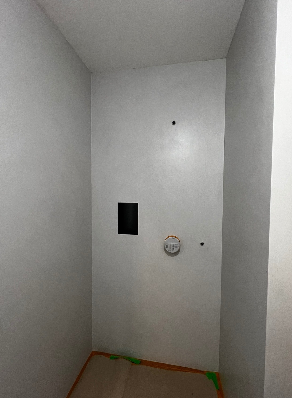 Wnętrze po szpachlowaniu ścian na gładko, widoczne otwory, zabezpieczona podłoga. Ściany w odcieniach szarości, przygotowane do malowania.