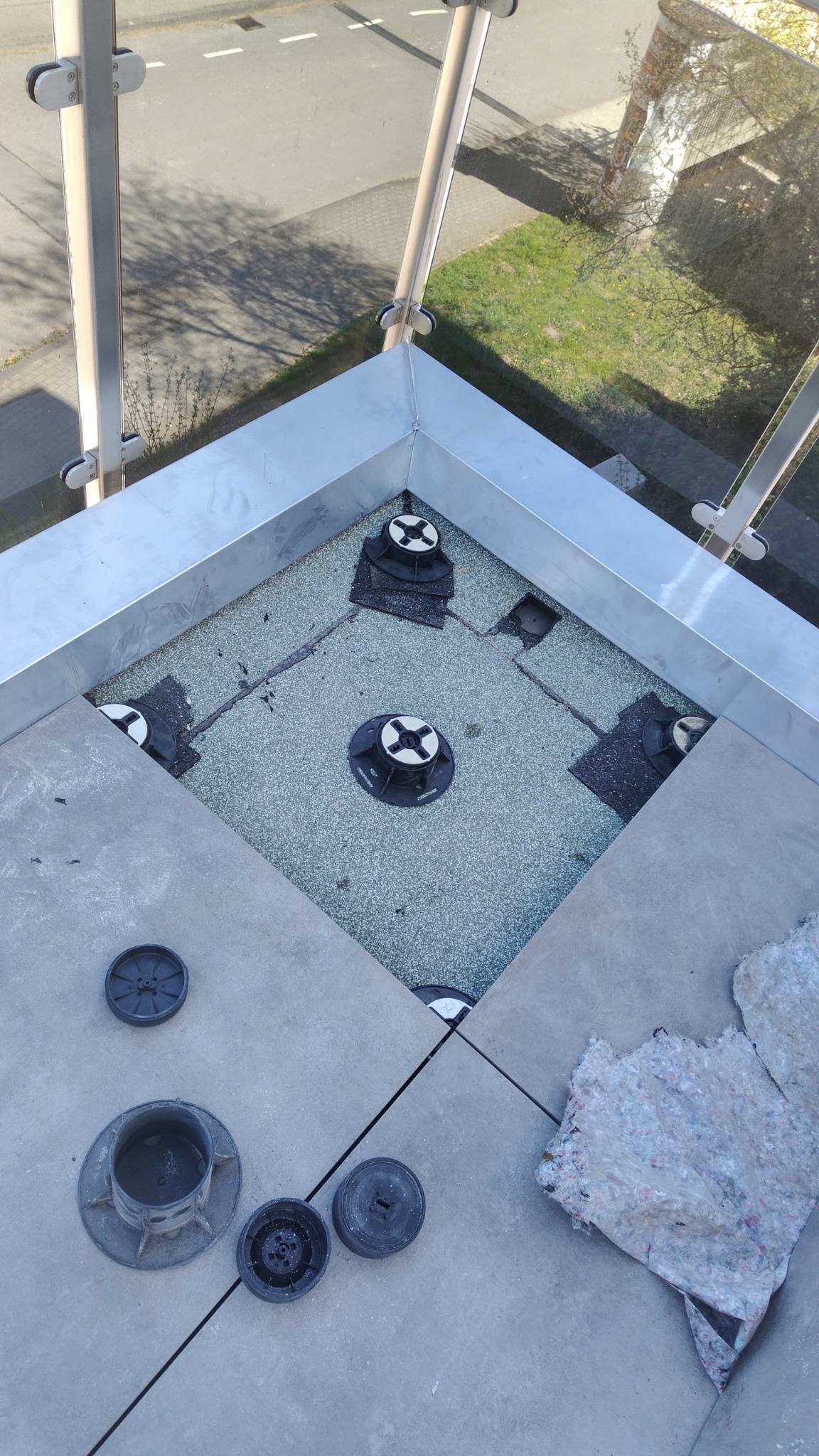 Montaż podestu tarasowego z regulowanymi wspornikami i płytami betonowymi. Widok z góry na fragment tarasu z balustradą i elementami montażowymi.