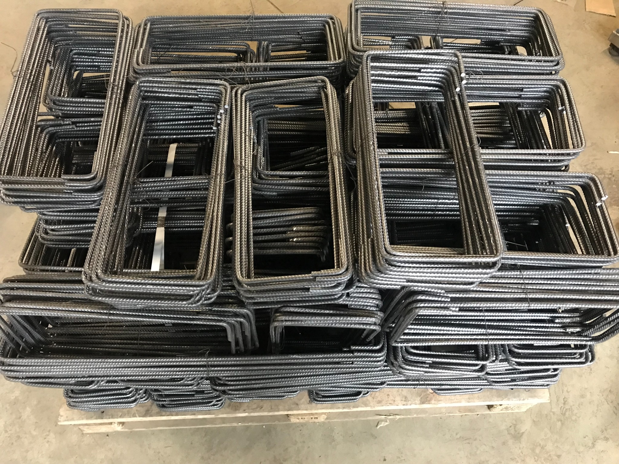 Stosy prostokątnych, metalowych prętów zbrojeniowych ułożonych na drewnianej palecie, widoczne z góry, z detalami faktury stali i wiązaniami drutem.