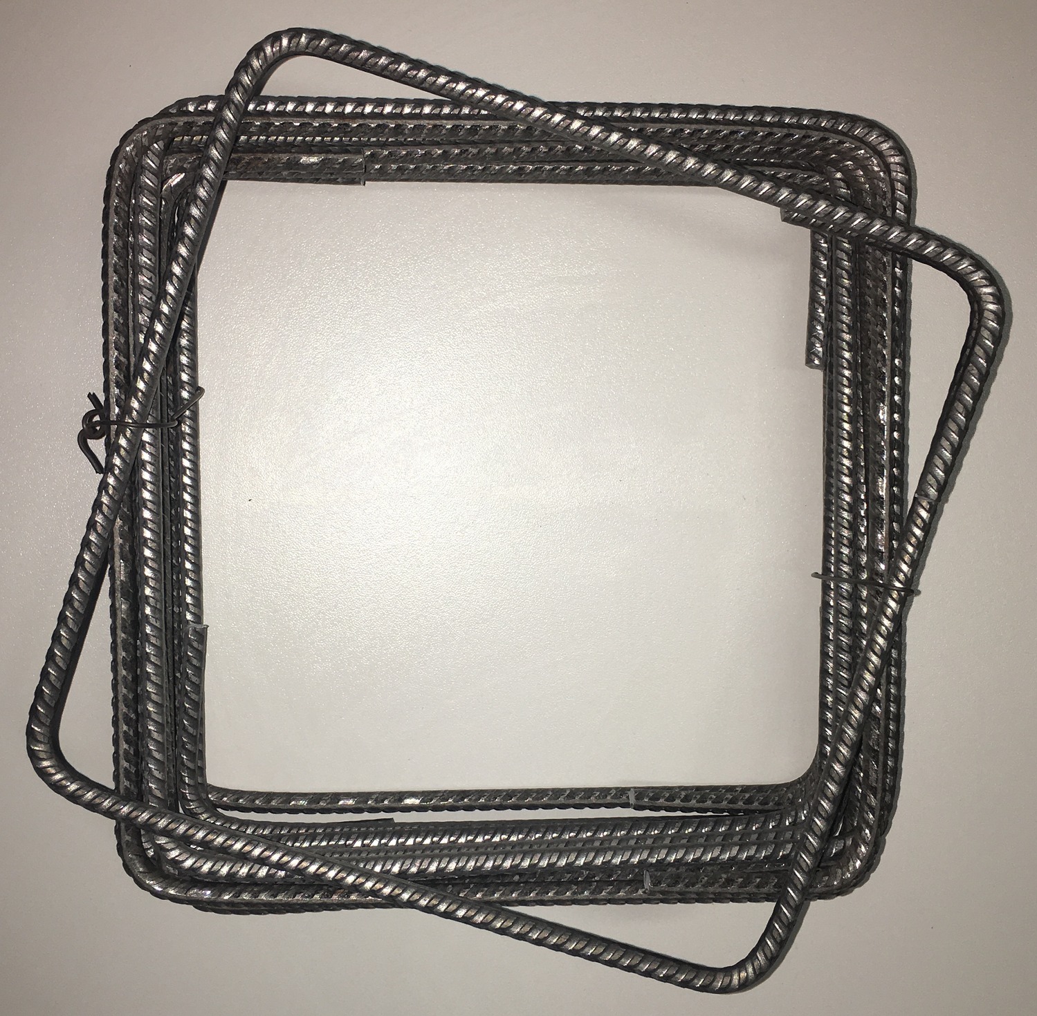 Kwadratowe, gotowe strzemiona z żebrowanej stali zbrojeniowej, spięte drutem, ułożone warstwami na jasnym tle. Widok z góry, ostre światło.