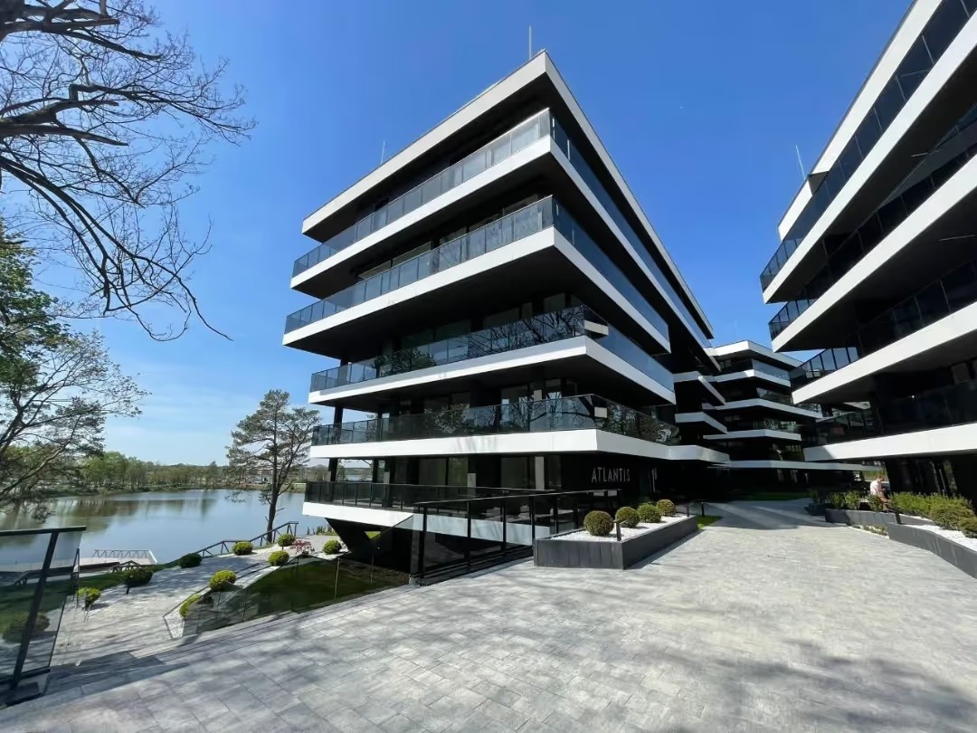 Nowoczesny apartamentowiec 'Atlantis' w Nasielsku z widokiem na jezioro, minimalistyczna architektura, biało-czarne elewacje, szara kostka brukowa na podejściu.