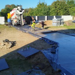 Zaczarowany ogród - Wylewka betonowa na posesji z użyciem betoniarki, widoczni pracownicy w trakcie rozprowadzania betonu. W tle ogrodzenie panelowe i drzewa.