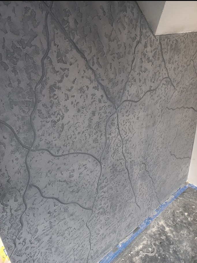 Szara ściana z unikalną fakturą i wzorem przypominającym żyły kamienia, wykonana techniką dekoracyjną. Widoczne detale wykończenia i oświetlenie podkreślające strukturę.