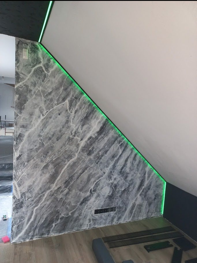 Ściana wykończona w stylu marmuru z podświetleniem LED w rogu, tworząca nowoczesny efekt w pomieszczeniu ze skośnym sufitem. Widoczne elementy grzejnika.