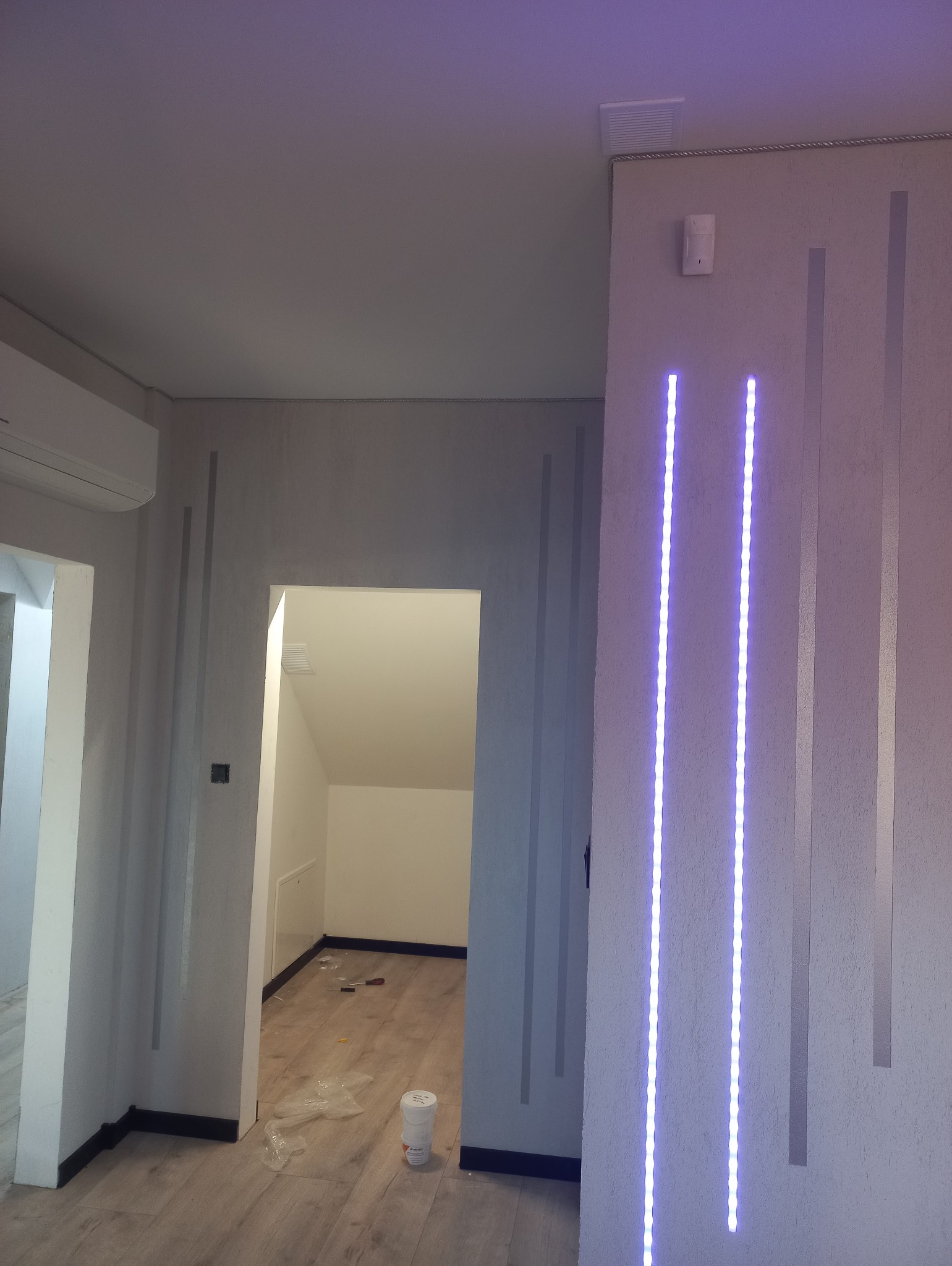 Wykończone wnętrze z dekoracyjnym oświetleniem LED na ścianie. Widoczne drzwi do innego pomieszczenia i elementy wykończeniowe pod sufitem.