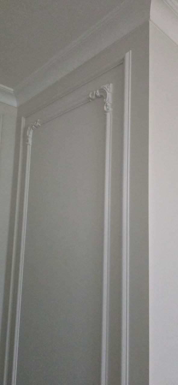 Eleganckie, białe sztukaterie zdobiące ścianę, z dekoracyjnymi narożnikami i subtelnymi listwami. Klasyczny detal wykończenia wnętrza.