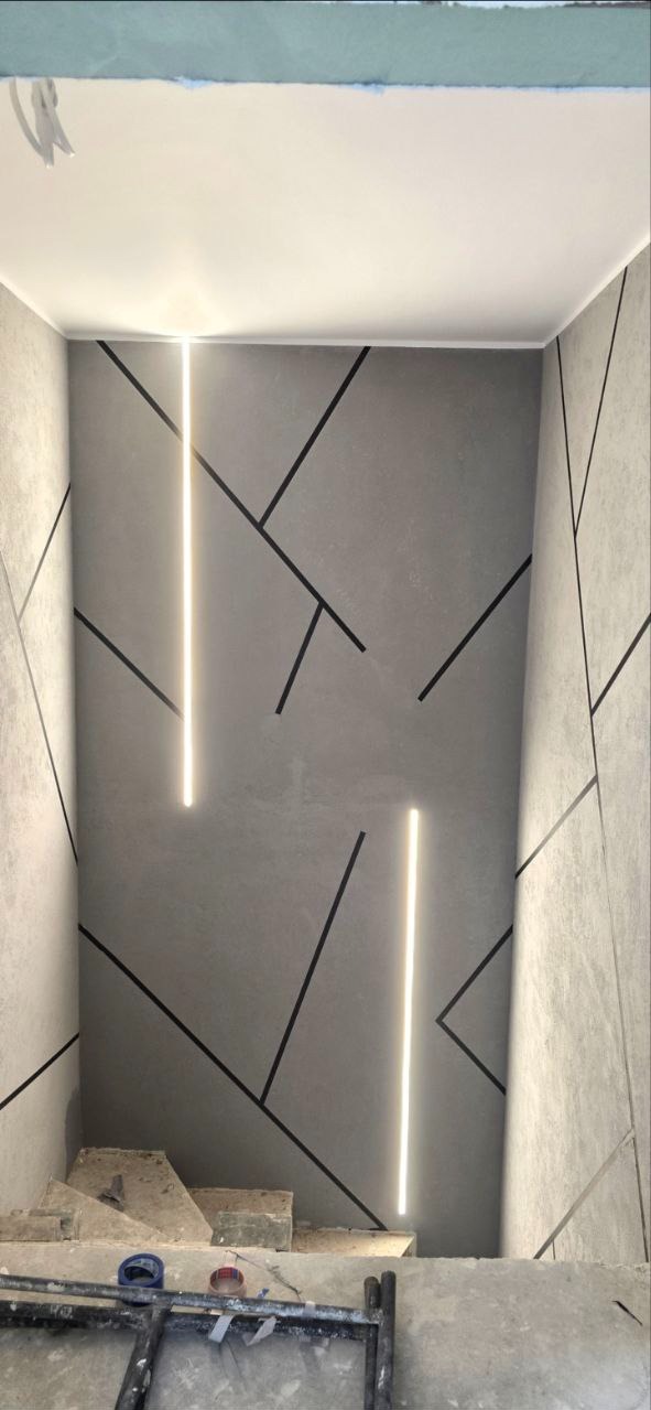 Szara ściana z geometrycznym wzorem i pionowymi paskami LED, widok z dołu, fragment rusztowania. Nowoczesne wykończenie wnętrza w trakcie realizacji.