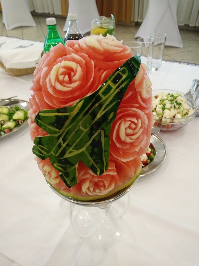 Arbuzowa rzeźba: róże i samolot na eleganckim stole z sałatkami. Unikalna dekoracja cateringowa na przyjęciu, prezentująca kunsztowne carvingi.