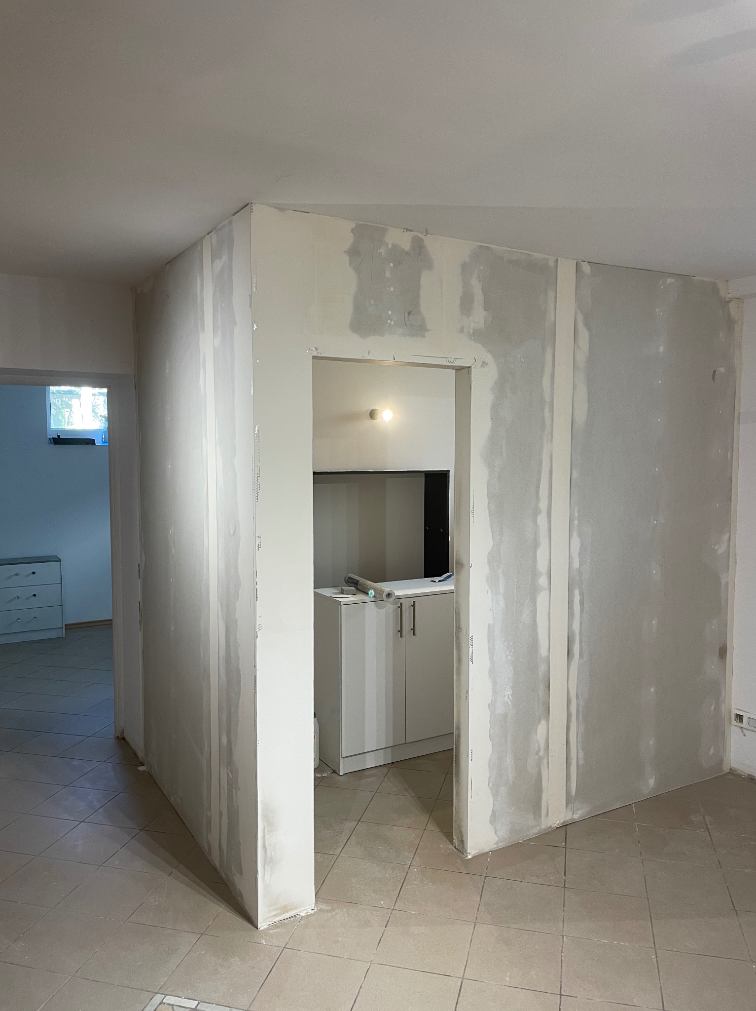 Wnętrze w trakcie prac: ściany z płyt karton-gips, widoczne łączenia i szpachlowanie. W tle fragment zabudowy kuchennej i otwarte przejście do innego pomieszczenia.