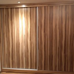 stanislaw werbowecki - Szafa przesuwna z drewnopodobnymi frontami, widoczne pionowe pasy w odcieniach brązu i beżu, srebrne prowadnice, na podłodze odkurzacz.