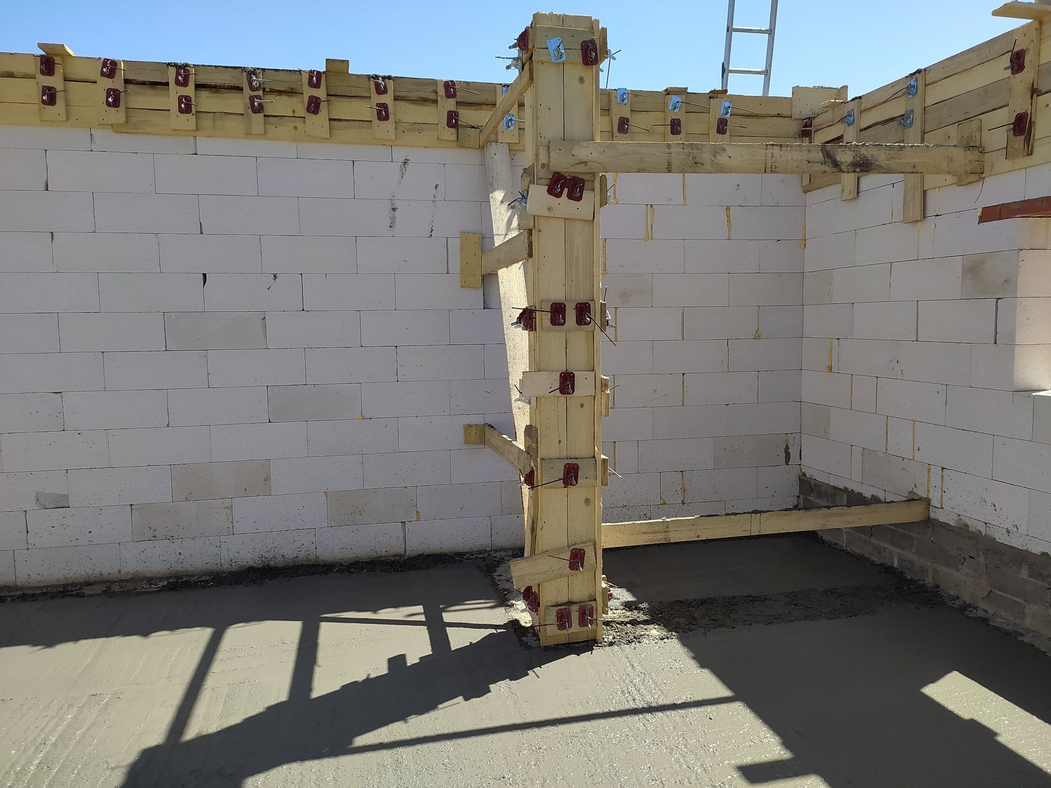 Murowanie ścian z betonu komórkowego, widoczne drewniane szalunki i świeżo wylana posadzka. Etap budowy domu jednorodzinnego w słoneczny dzień.