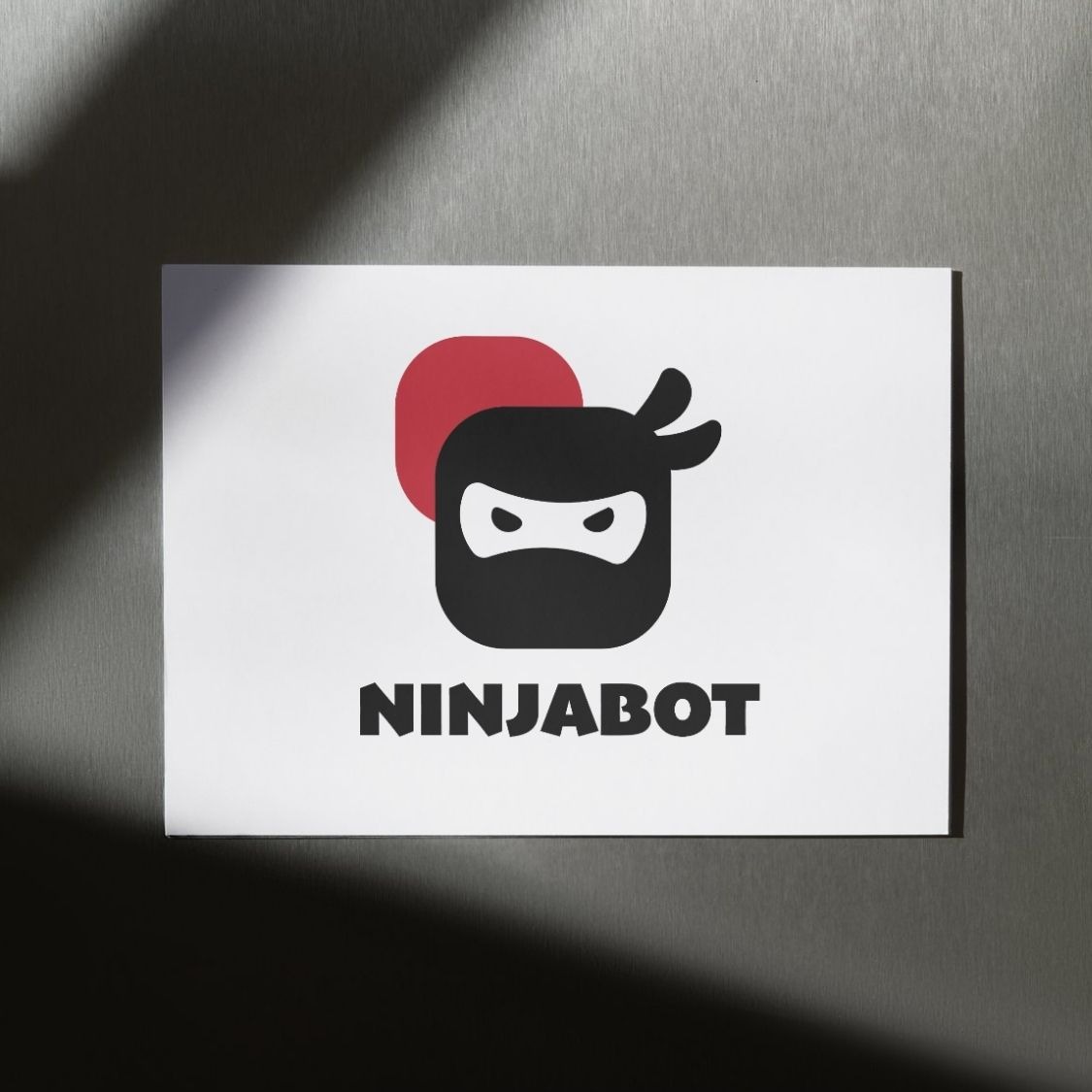 Minimalistyczne logo 'Ninjabot' z motywem ninja i czerwonym okręgiem w tle, umieszczone na białej kartce z cieniem, na metalowym tle.