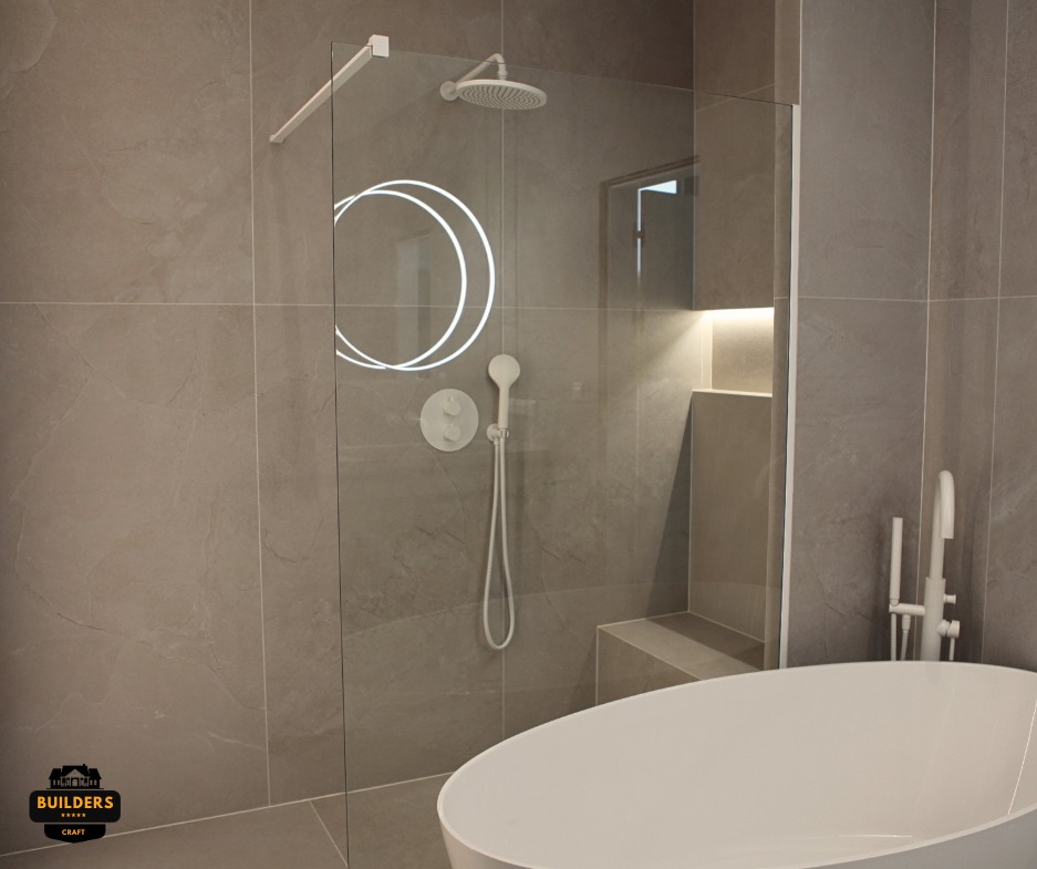 Nowoczesna łazienka z szarymi płytkami, kabiną prysznicową typu walk-in z podświetlanym panelem i wolnostojącą białą wanną. Minimalistyczny design.