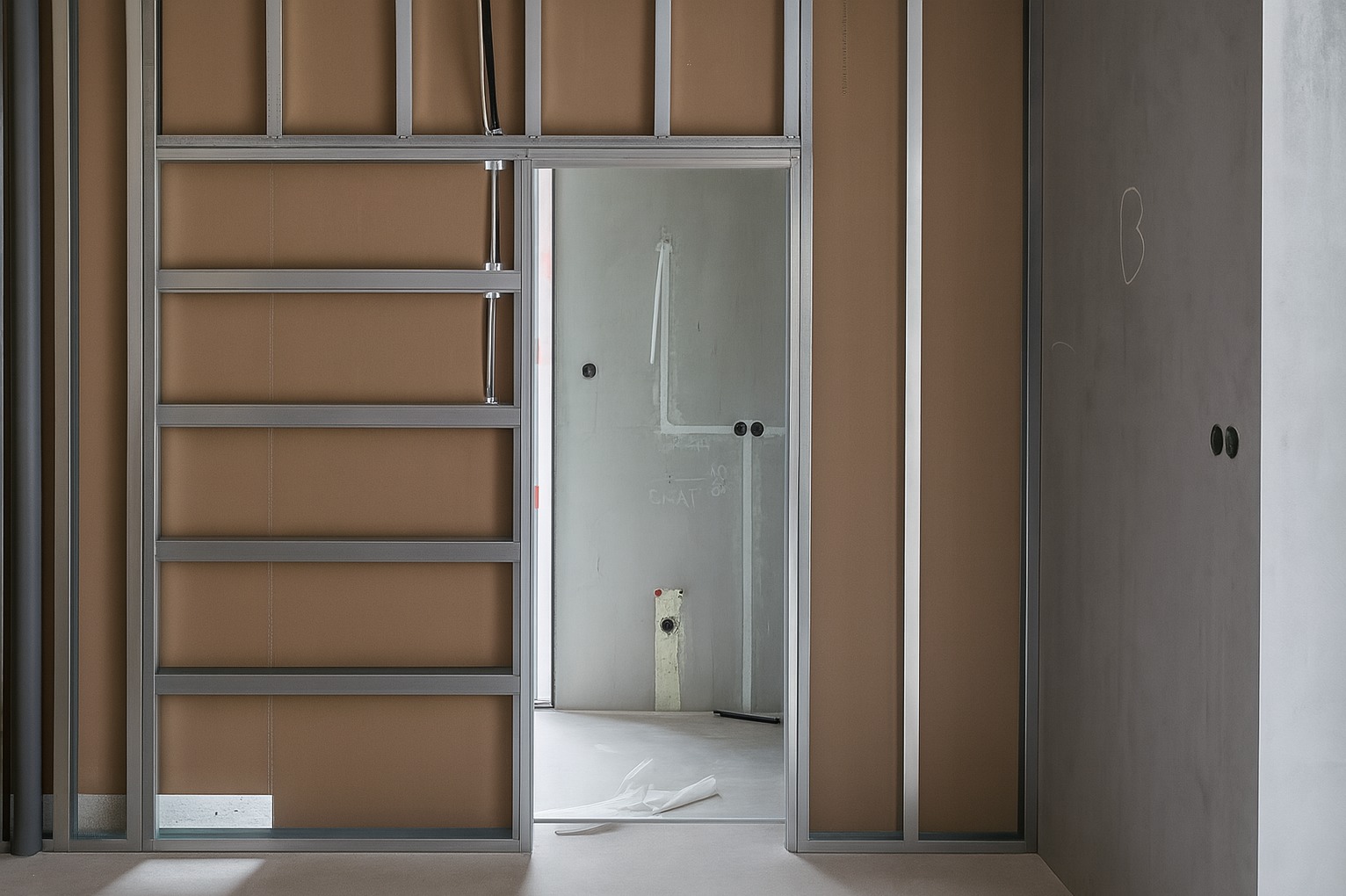 Wnętrze w trakcie prac wykończeniowych: metalowa konstrukcja ścian działowych z płytami, widoczne instalacje. Surowy stan, przygotowanie do dalszych prac.