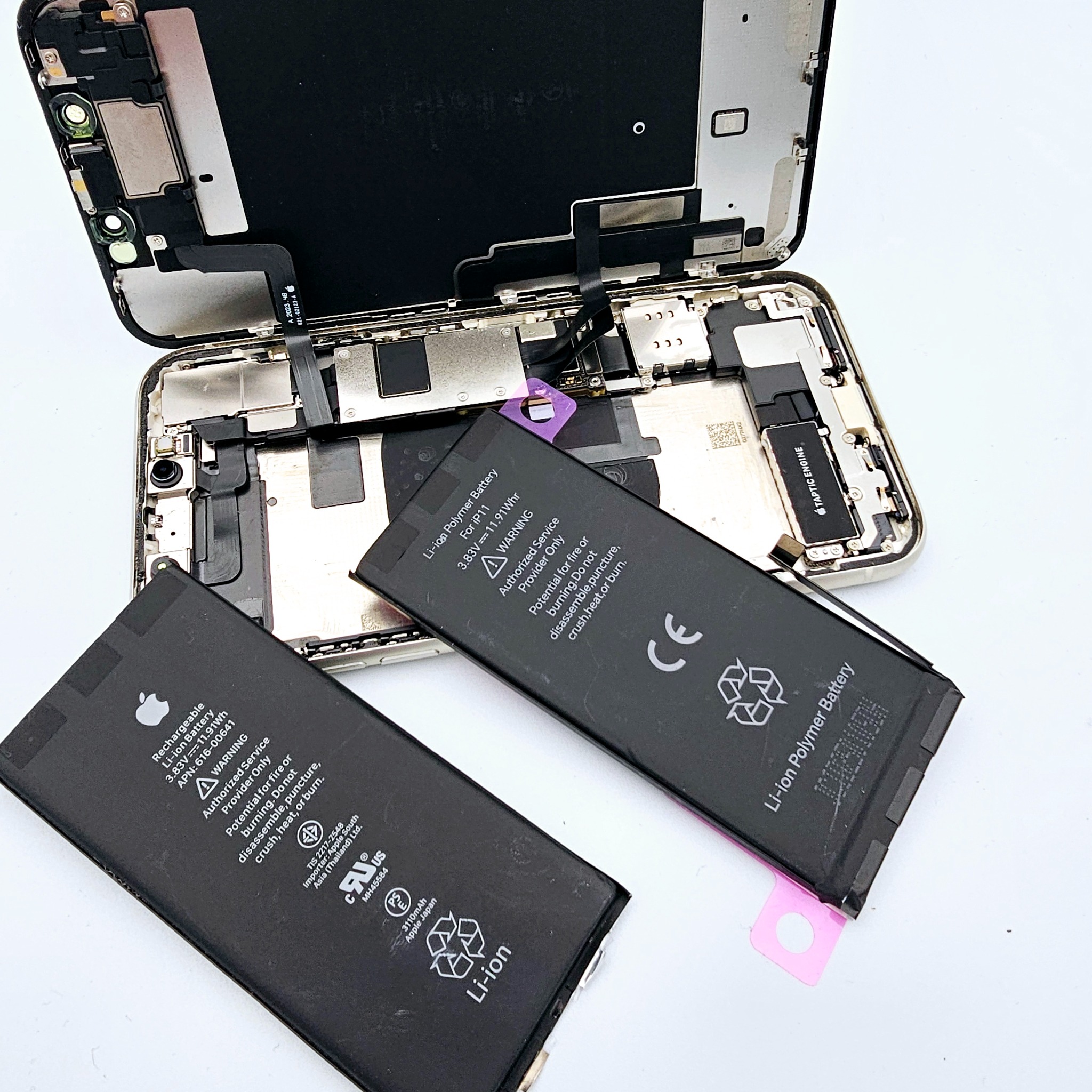 Rozłożony iPhone 11 z widocznymi bateriami i elementami wewnętrznymi. Baterie leżą obok obudowy. Widoczne oznaczenia na bateriach.