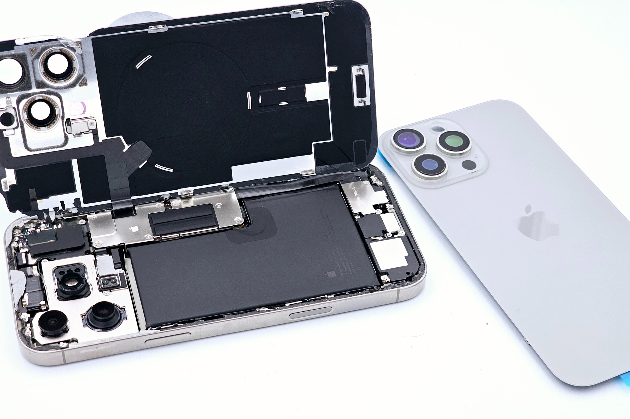 Rozłożony iPhone 13 Pro Max na białym tle, widoczna bateria, płyta główna i tylna obudowa. Ukazany etap naprawy lub demontażu telefonu.