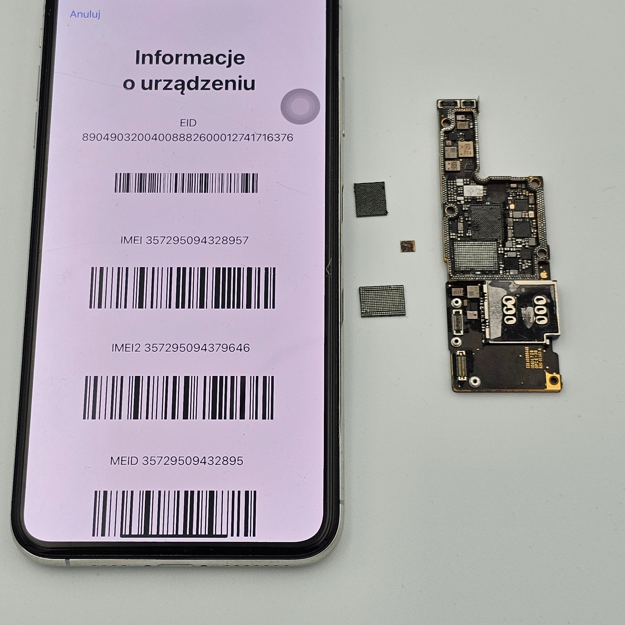Smartfon z wyświetlonymi informacjami o urządzeniu (IMEI, EID) obok rozłożonej płyty głównej i układów scalonych. Diagnostyka i naprawa telefonów.