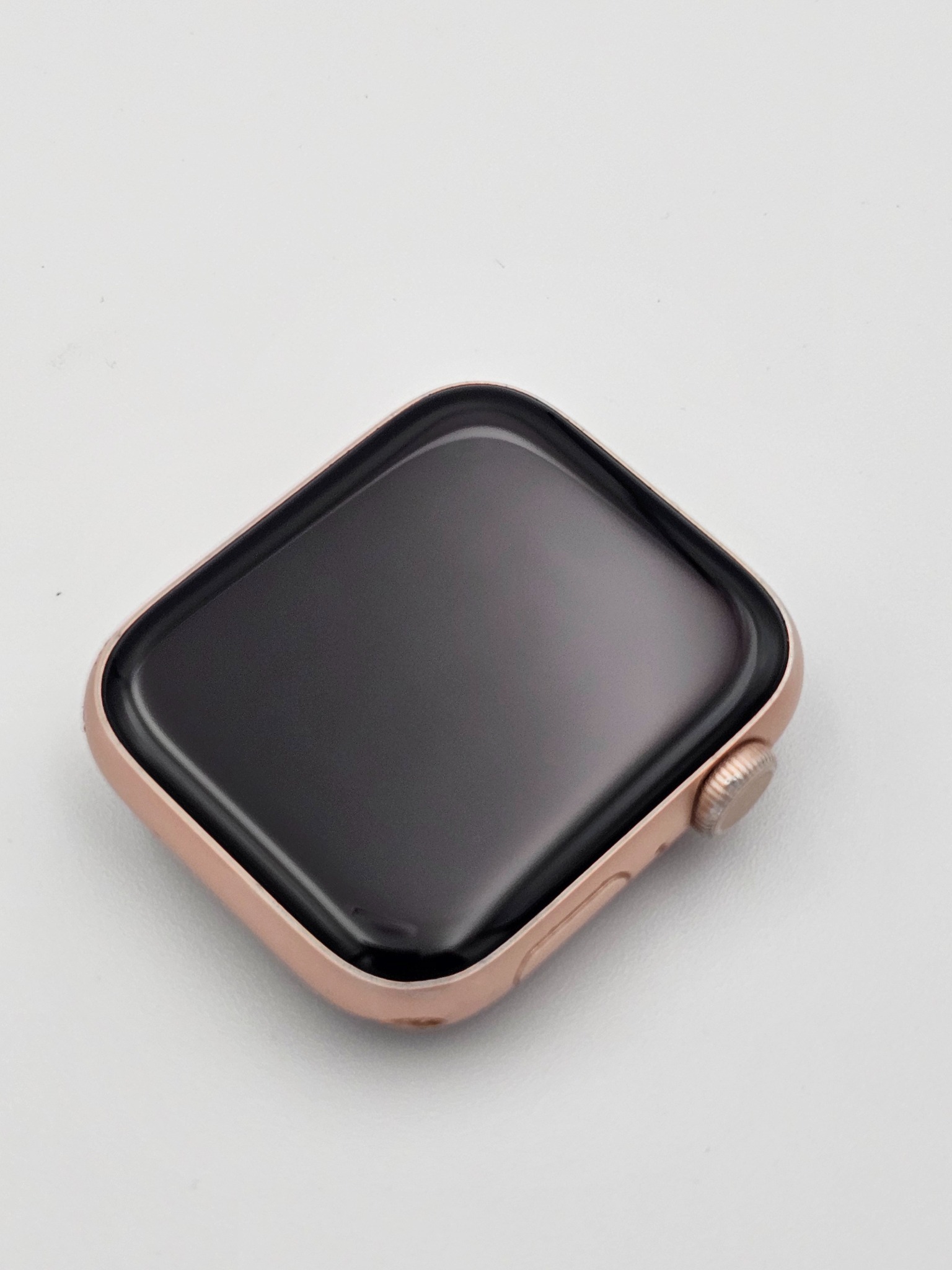 Złoty smartwatch z czarnym ekranem, leżący na białym tle. Widoczny przycisk boczny. Minimalistyczne ujęcie z góry, skupiające się na detalu urządzenia.