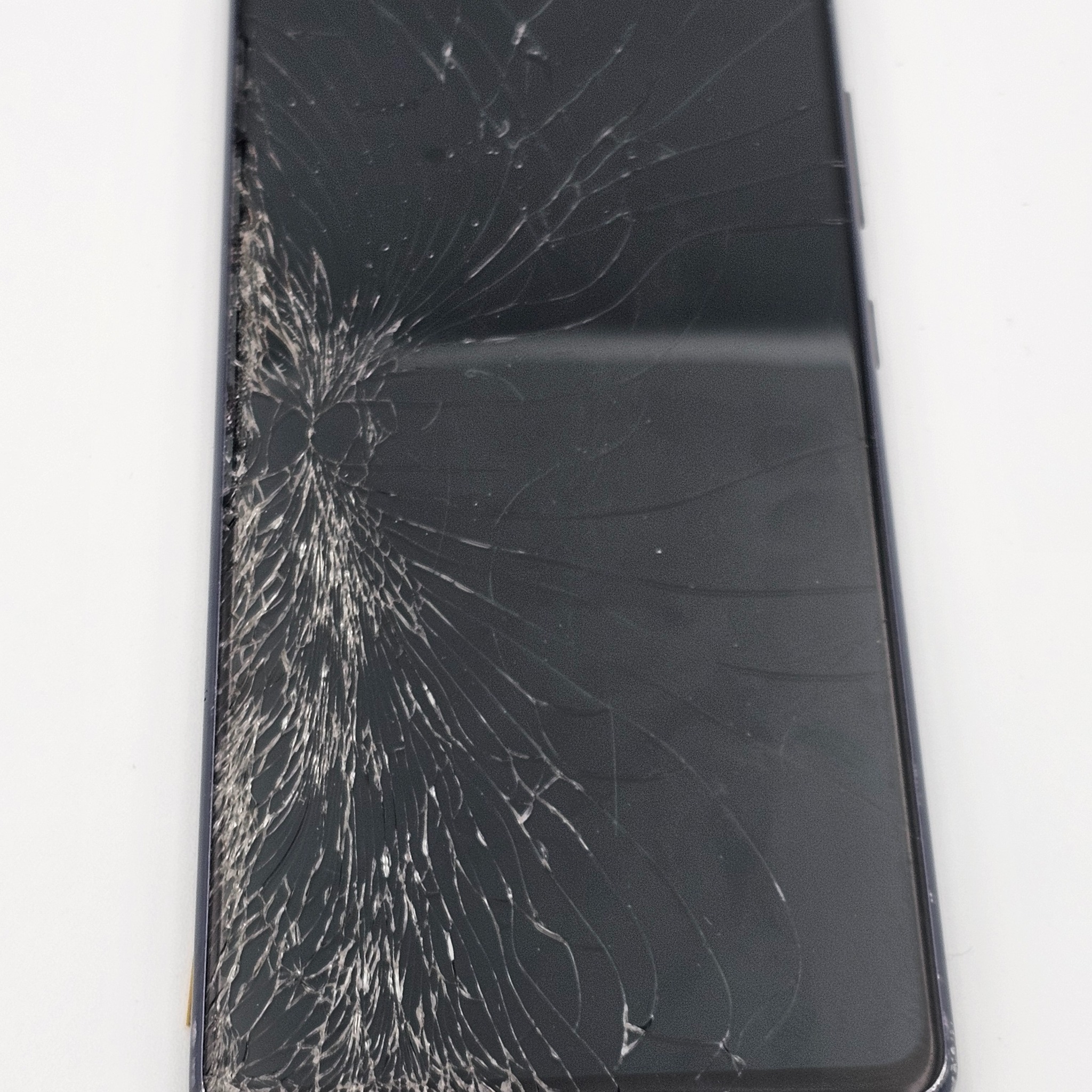 Smartfon z pękniętym ekranem na białym tle. Liczne pajęczynowe pęknięcia szkła. Uszkodzony wyświetlacz telefonu komórkowego.