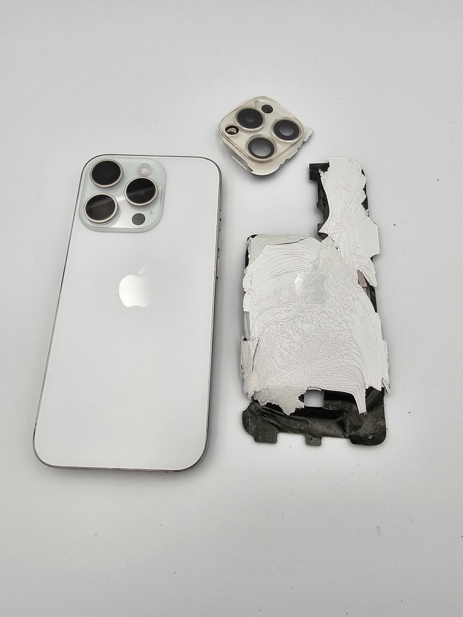 Uszkodzony iPhone 13 Pro Max w kolorze białym, z odklejoną obudową i osłoną aparatu. Widoczne ślady kleju i uszkodzenia. Prezentacja naprawy telefonu.