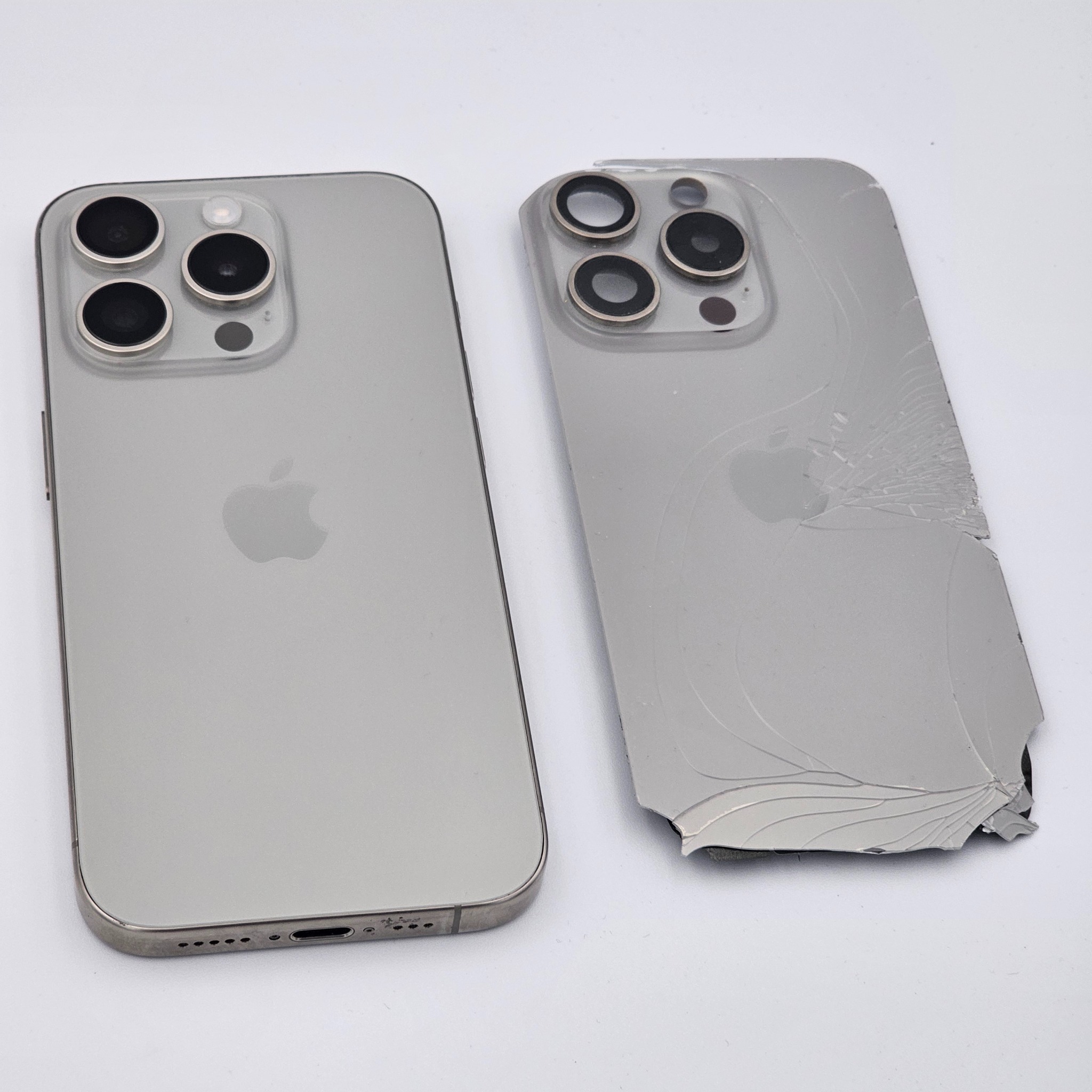 Uszkodzony iPhone 13 Pro Max z pękniętą obudową obok sprawnego modelu, ukazujący zakres naprawy. Widoczne cztery obiektywy aparatu i logo Apple.