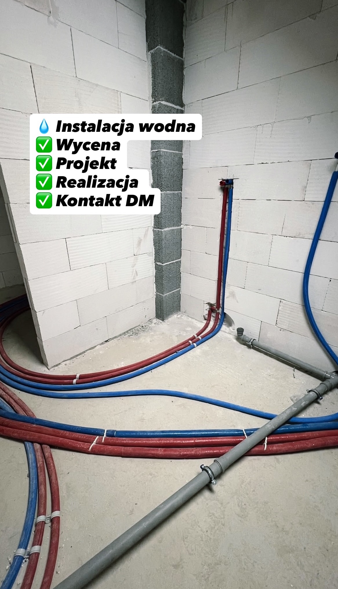 Instalacja wodna w surowym wnętrzu: czerwone i niebieskie rury prowadzone wzdłuż ściany z betonu komórkowego, widoczne przyłącza. Etap prac przed wykończeniem.