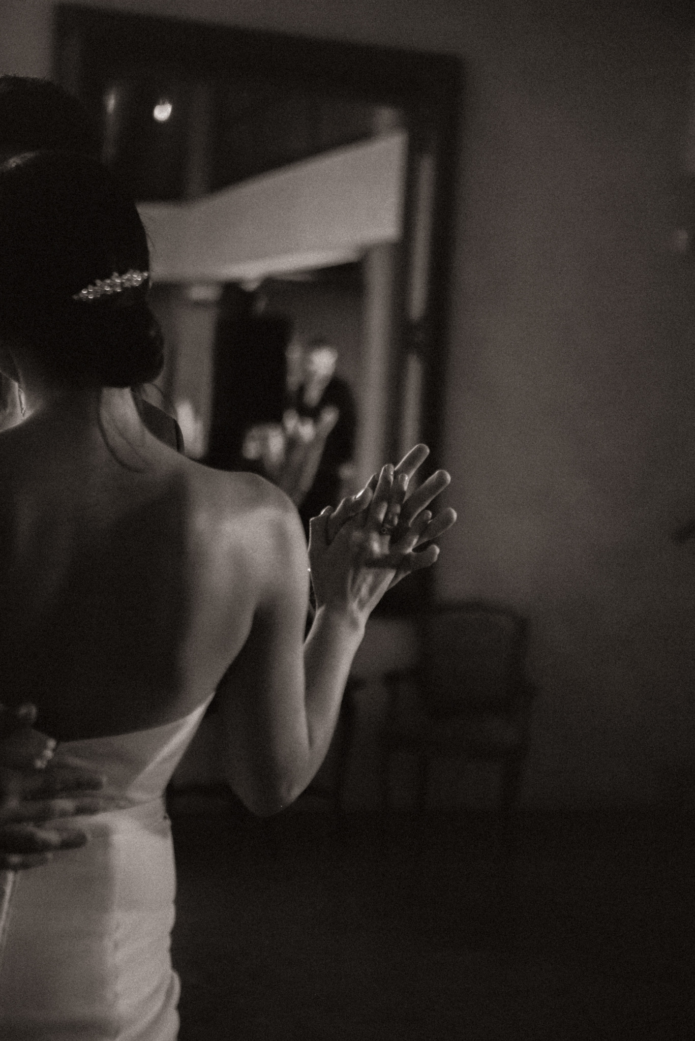 Czarno-białe zdjęcie panny młodej w sukni bez ramiączek, trzymającej dłoń partnera podczas pierwszego tańca, z odbiciem pary w lustrze w tle.