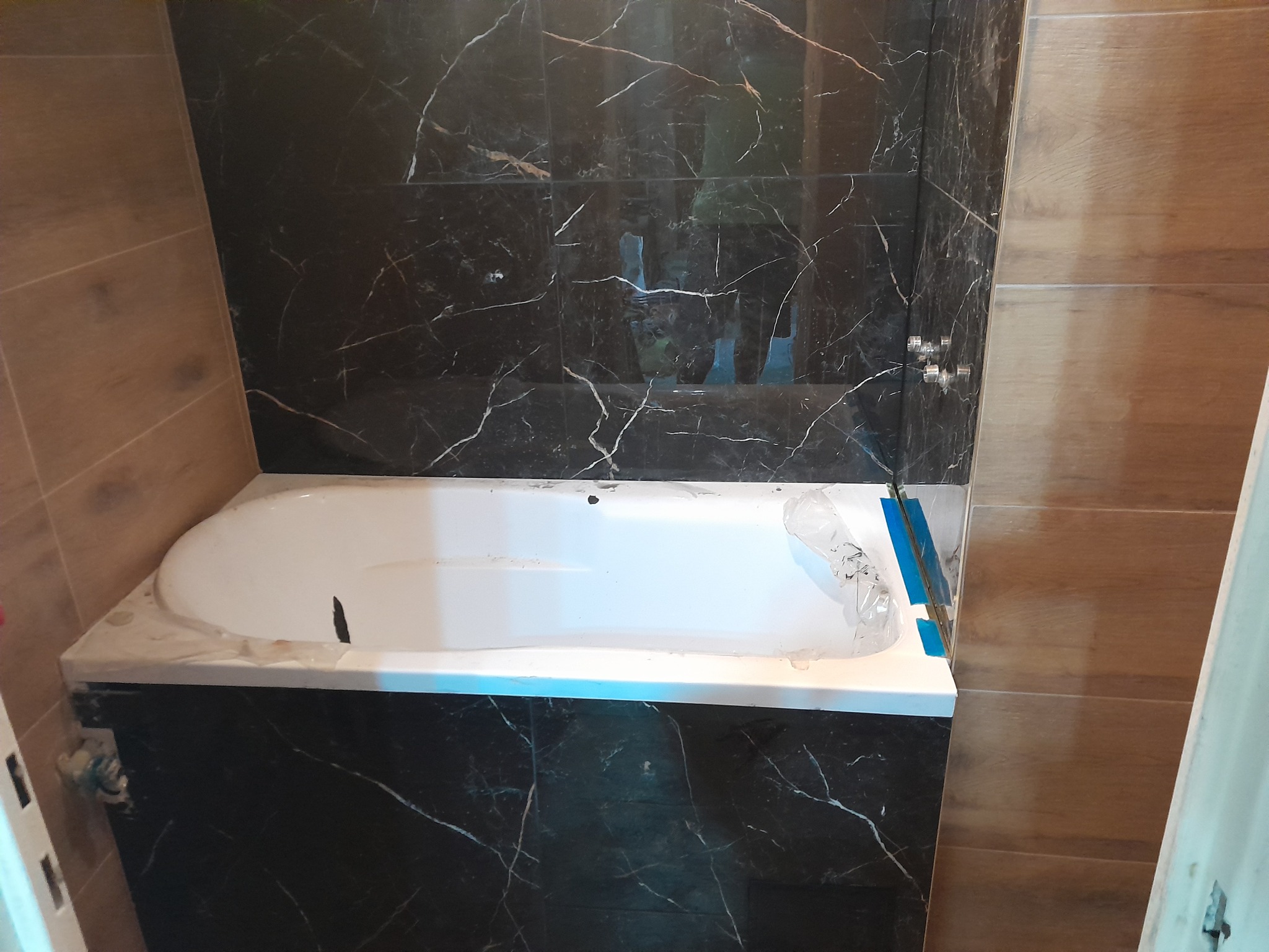 Wykończona obudowa wanny z czarnych płytek imitujących marmur, brązowe płytki na ścianie, widoczne baterie. Nowoczesny design łazienki po remoncie.