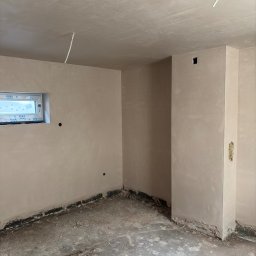 Sar-Bud - Świeżo otynkowane ściany i sufit w pomieszczeniu w Koszwicach, z oknem VEKA, wystającymi przewodami elektrycznymi i surową, brudną podłogą z cegłami.