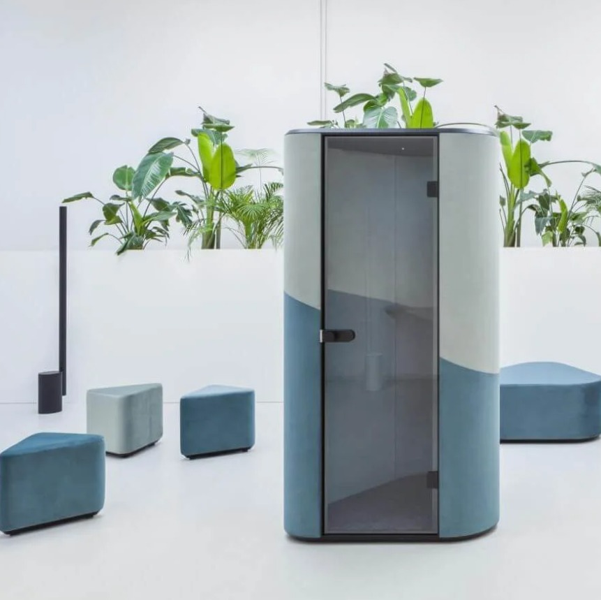 Nowoczesna, wyciszona kabina biurowa z przeszkleniem, otoczona zielenią i siedziskami w odcieniach błękitu, na tle białej przestrzeni biurowej.
