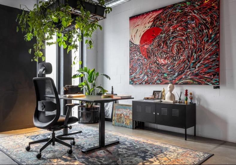 Nowoczesne biuro w Krakowie z regulowanym biurkiem, ergonomicznym krzesłem i abstrakcyjnym obrazem. Rośliny doniczkowe dodają świeżości.