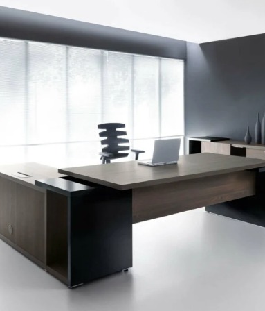 Nowoczesne biuro z dużym, drewnianym biurkiem, laptopem i krzesłem na tle okna z żaluzjami. Minimalistyczny design w szarościach i bieli.