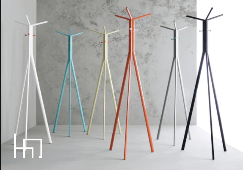 Kolorowe, nowoczesne wieszaki stojące na ubrania, ustawione w rzędzie na tle szarej ściany. Minimalistyczny design, różne barwy: biały, turkusowy, żółty, pomarańczowy, szary i czarny.