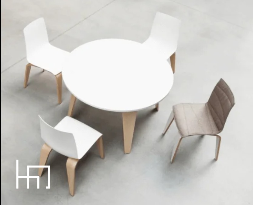 Biały okrągły stół otoczony czterema krzesłami (trzy białe, jedno tapicerowane) na jasnej podłodze, widok z góry, minimalistyczny design.