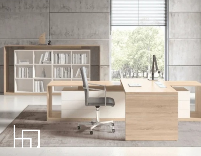 Nowoczesne biuro z biurkiem z drewna, regałem na książki i szarym krzesłem obrotowym na tle betonowej ściany i okna z widokiem na zieleń.