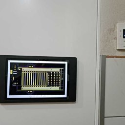 KRC TRADING GROUP SP. Z O.O. - Tablet z schematem instalacji na ścianie obok panelu sterowania. Układ elektroniczny na ekranie, nowoczesne sterowanie, białe ściany, minimalistyczny design.
