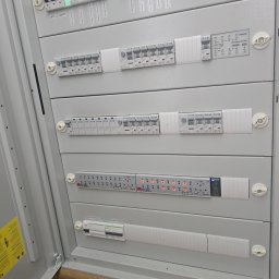 KRC TRADING GROUP SP. Z O.O. - Szara szafa rozdzielcza z bezpiecznikami i modułami KNX, widoczne oznaczenia obwodów i diody sygnalizacyjne. Instalacja elektryczna wewnątrz szafy.