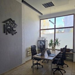 KRC TRADING GROUP SP. Z O.O. - Nowoczesne biuro z logo firmy KRC na ścianie, stołem konferencyjnym z laptopami i drukarką 3D w tle. Minimalistyczny design, duże okno z widokiem na zewnątrz.