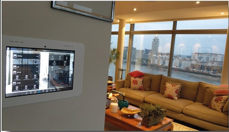 Panel sterowania inteligentnym domem na ścianie, obok widok na salon z dużym oknem i panoramą miasta. Nowoczesne rozwiązanie dla komfortu i bezpieczeństwa.