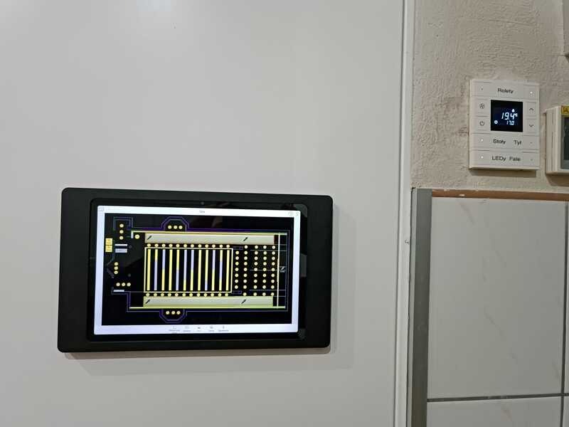 Tablet z schematem instalacji na ścianie obok panelu sterowania. Układ elektroniczny na ekranie, nowoczesne sterowanie, białe ściany, minimalistyczny design.