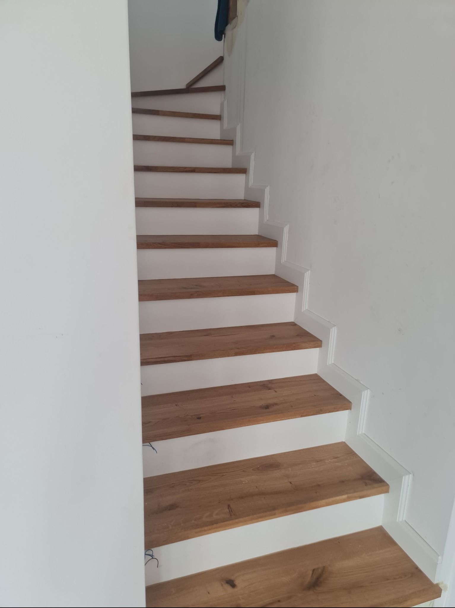 Schody z drewnianymi stopniami i białymi podstopnicami w Pabianicach. Widok z dołu, ukazujący detale wykończenia i naturalny odcień drewna.